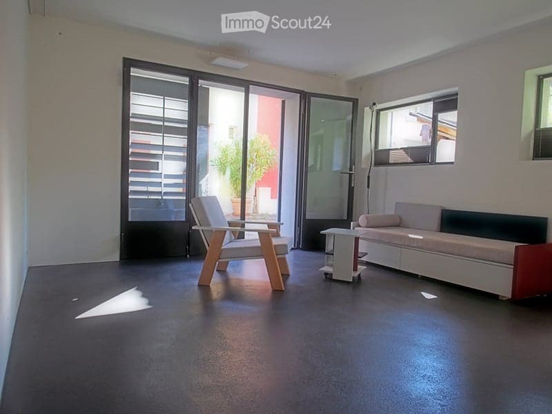 Modern living room with large glass doors leading to a patio, a white sofa, a wooden chair, and a small table.