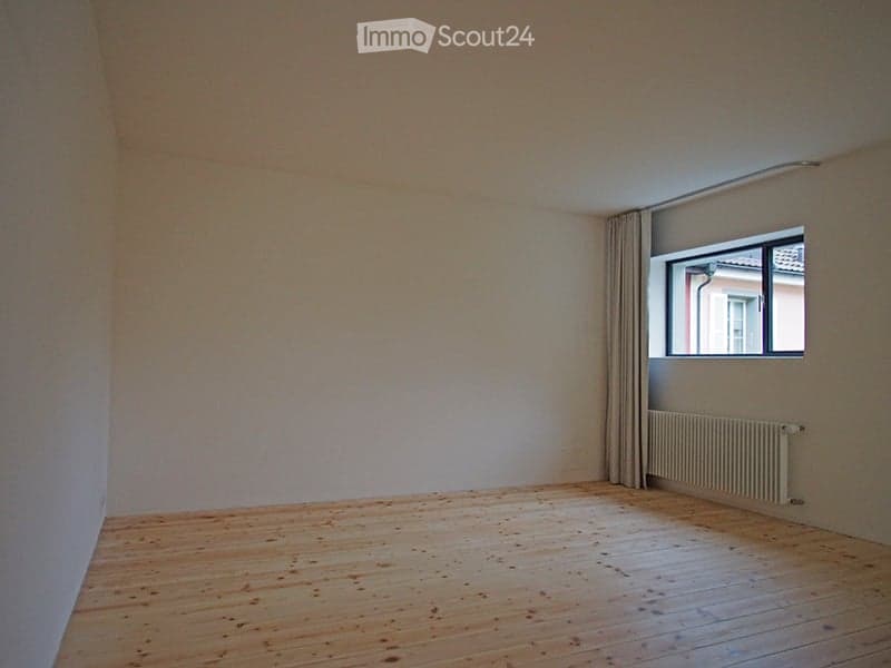 Empty room with wooden flooring, white walls, and a single window with a curtain. No furniture or equipment is present.