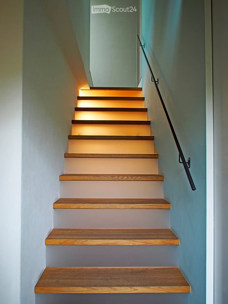 Modern staircase with wooden steps and a sleek black handrail, illuminated by warm ambient lighting.