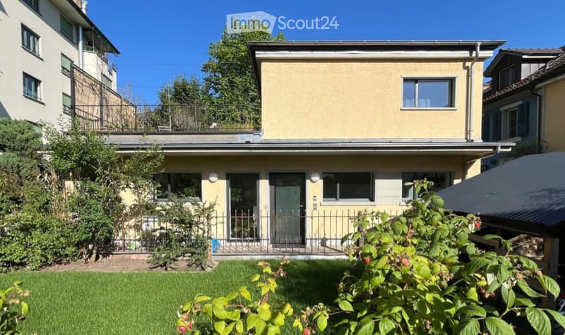 Two-story house with yellow exterior, multiple windows, and a small garden in front.