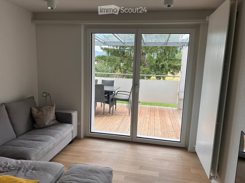 Living room with grey sofa, ottoman, and sliding glass doors leading to a balcony with outdoor furniture.