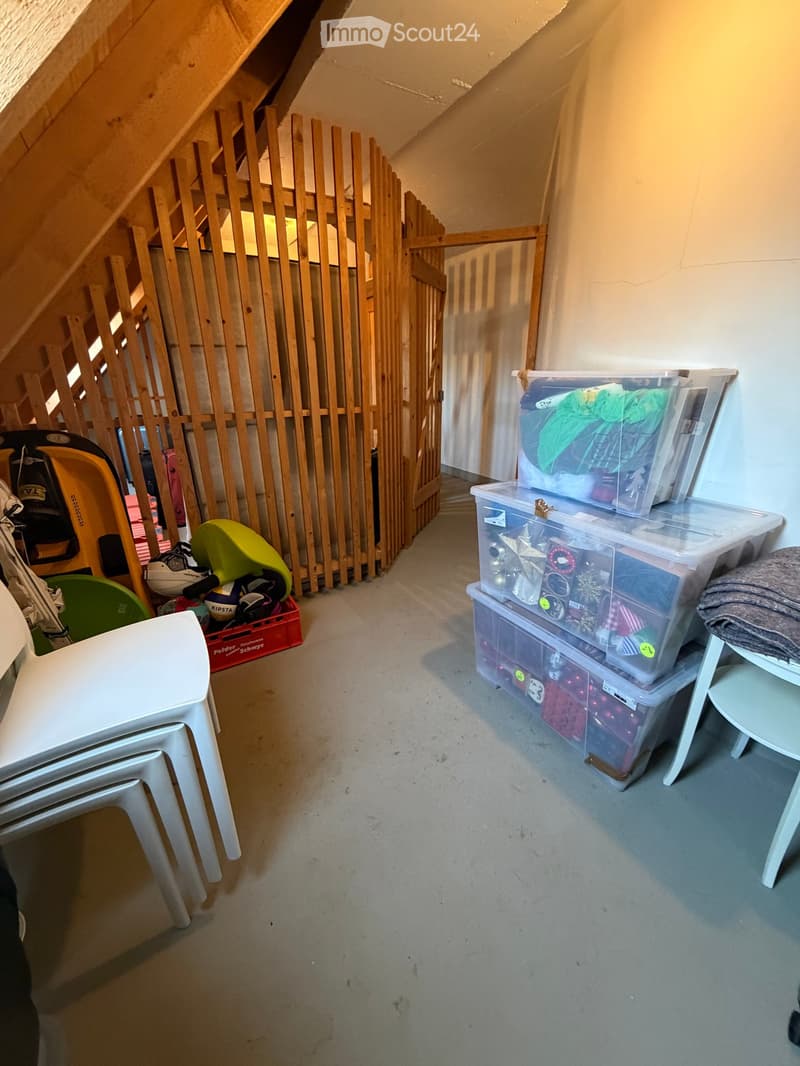 Storage room with wooden ladder, wooden fence, stack of plastic containers, white chairs, white shelf, red crate, umbrella, bags, shoes