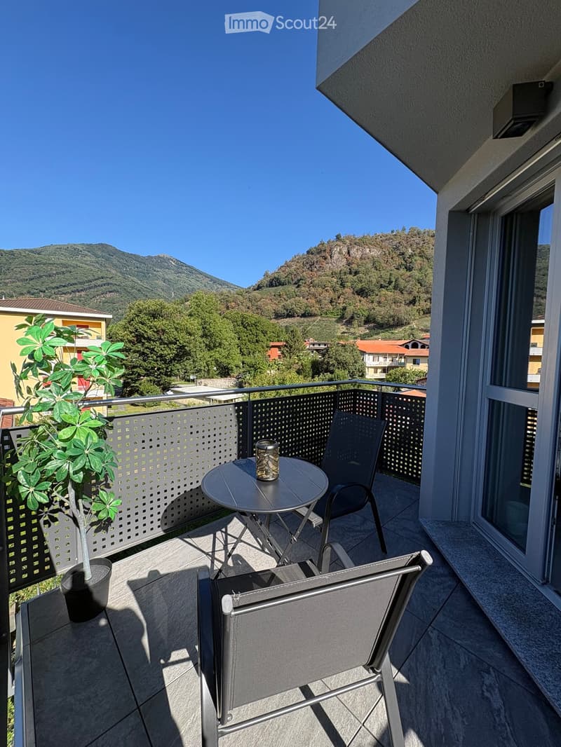 Balcony with a round table, two chairs, and a potted plant, overlooking a scenic mountain view.