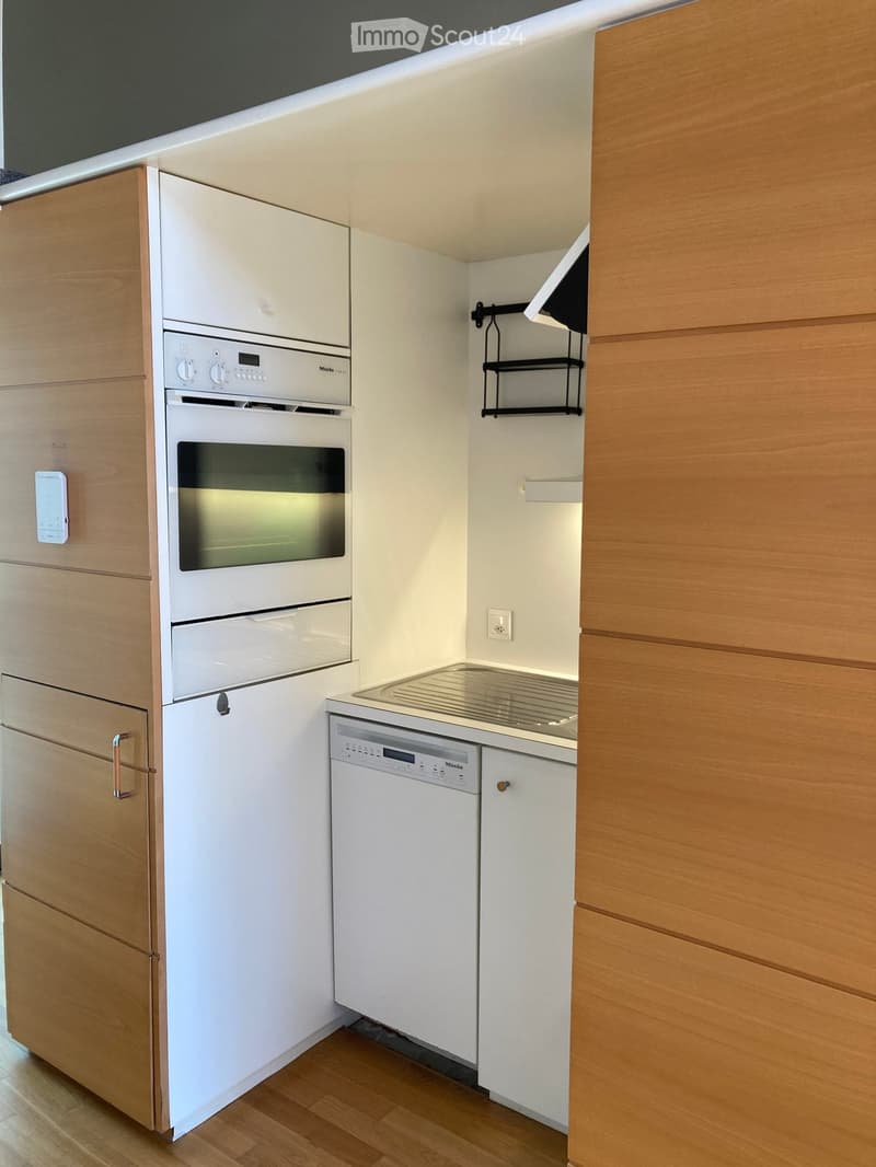 Modern kitchen with white appliances, wooden cabinets, and a stainless steel countertop.