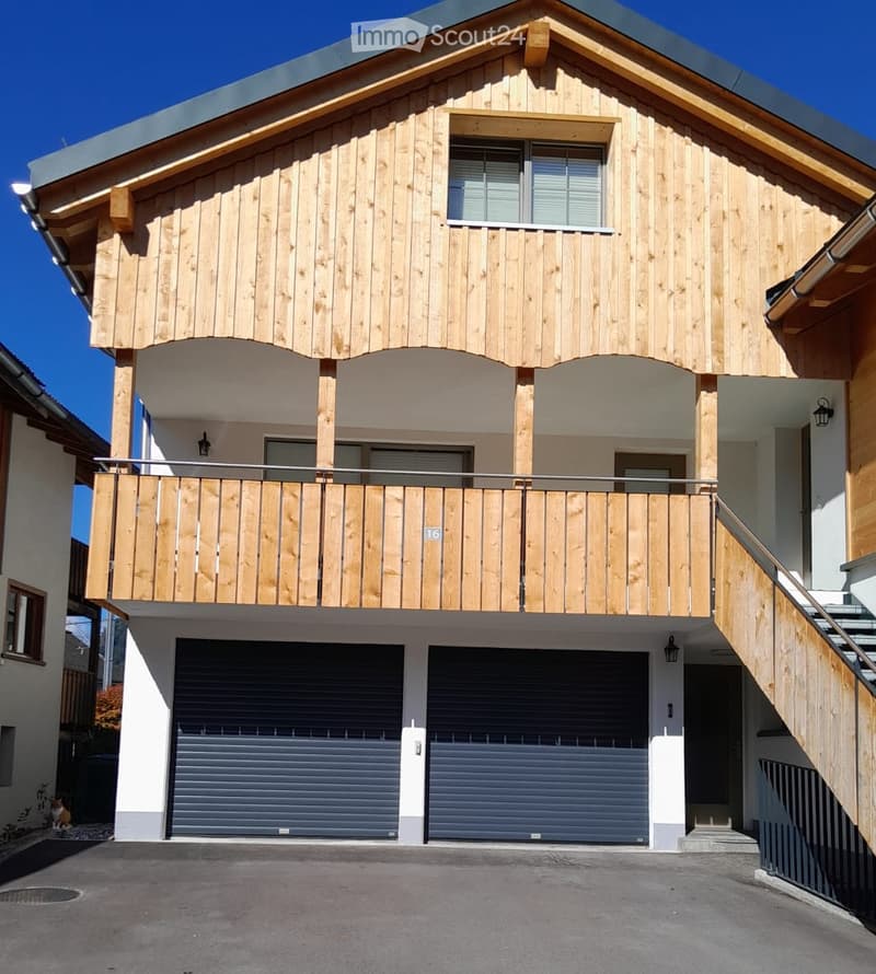 Two-story wooden house with a balcony, garage, and modern design.