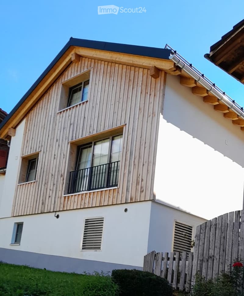 Two-story house with a combination of wooden and white siding, featuring multiple windows and a balcony on the upper level.