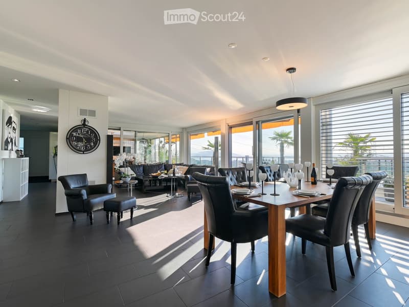 Modern dining and living area with dark tiled flooring, large windows, a dining table with chairs, a sofa, coffee table, and decorative items.
