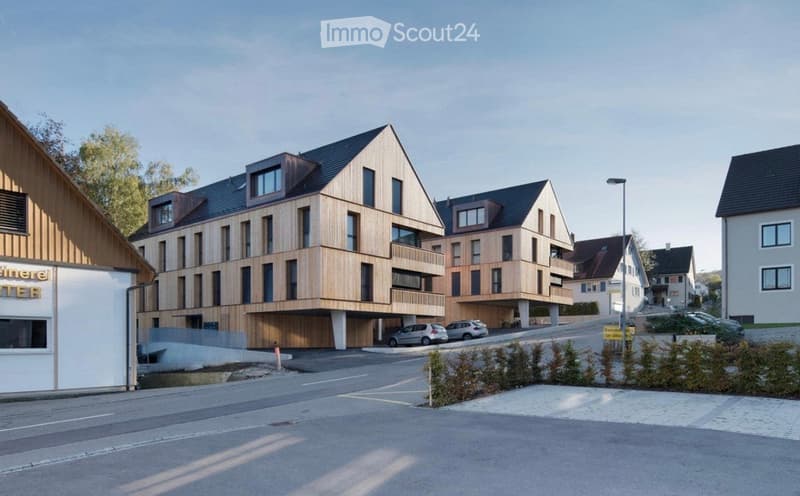 Modern multi-story residential building with wooden facade, balconies, and a covered parking area.