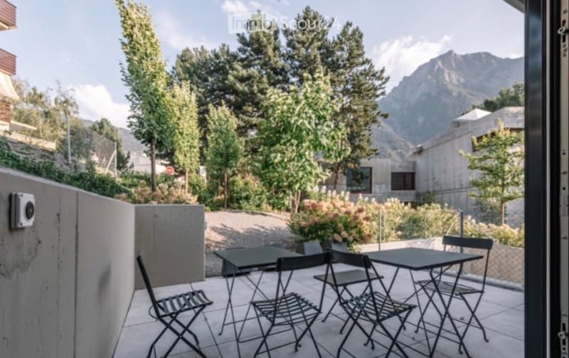 Balcony with outdoor furniture, overlooking a landscaped garden and mountain view.