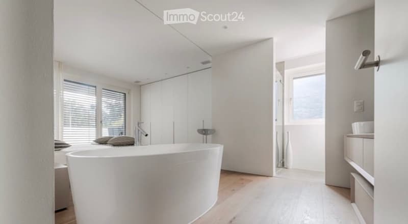 Modern bathroom with a freestanding bathtub, sleek faucet, built-in cabinetry, and decorative vases near the window.