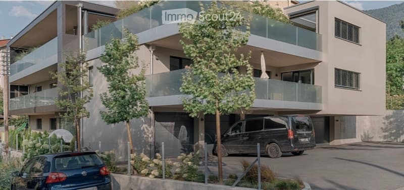 Modern multi-story apartment building with balconies, garage, and parking area.