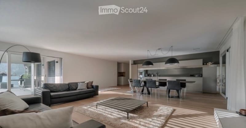 Modern open-plan living and dining area with a black leather sofa, coffee table, dining table with chairs, and sleek kitchen cabinets.
