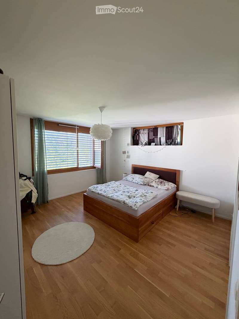 Cozy bedroom with wooden flooring, a double bed with patterned bedding, a round white rug, a small bench, and a pendant light fixture.