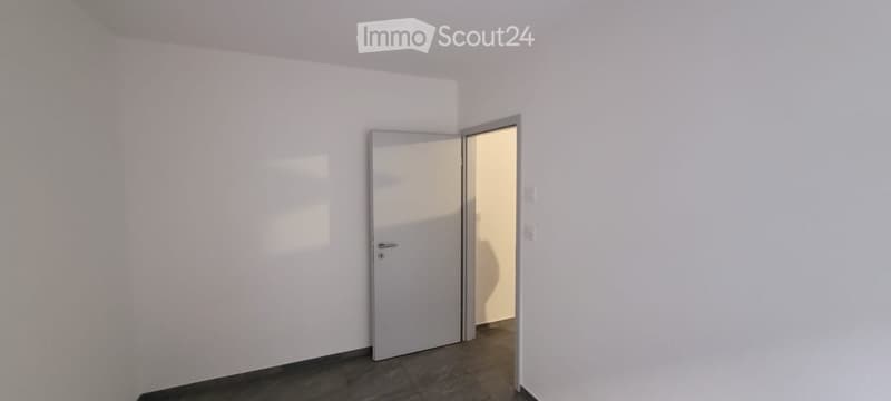 Empty room with white walls and dark tiled floor, featuring a closed door and an open doorway leading to another room.