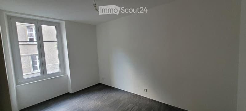 Empty room with light grey walls, wooden floor, and a large window with white frame. No furniture or equipment present.
