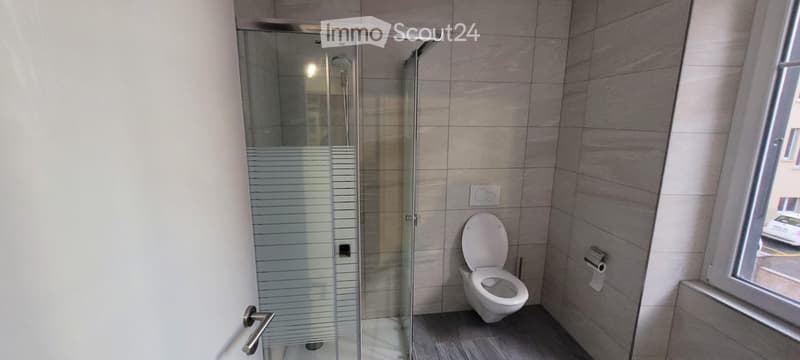 Modern bathroom with a glass-enclosed shower, toilet, and a window offering a view of the street.