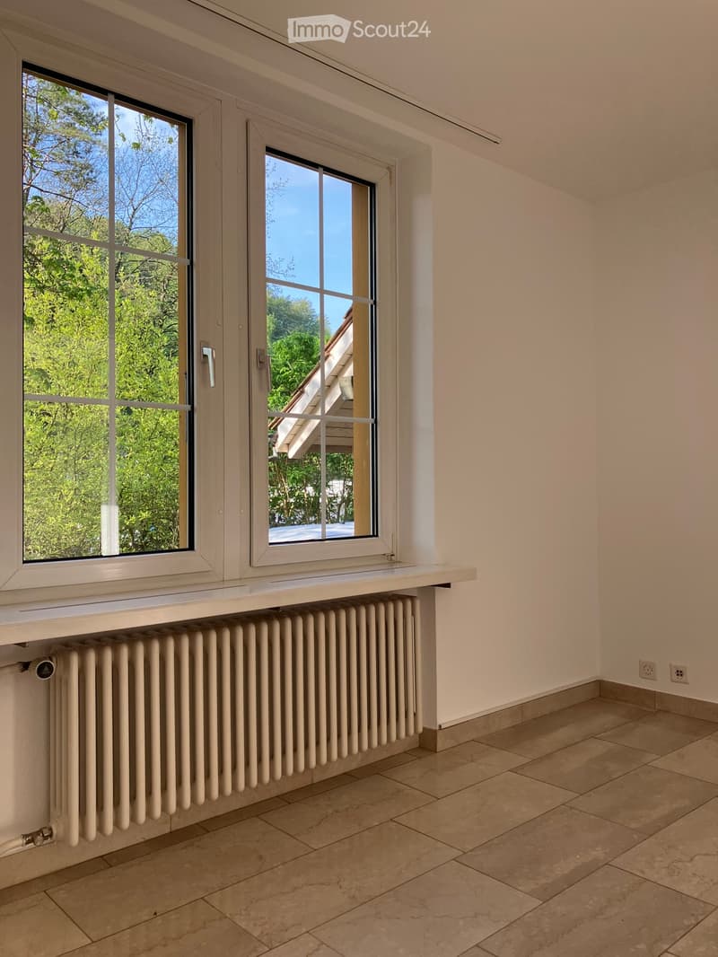 Empty room with tiled floor, white walls, large windows, radiator, and power outlets.