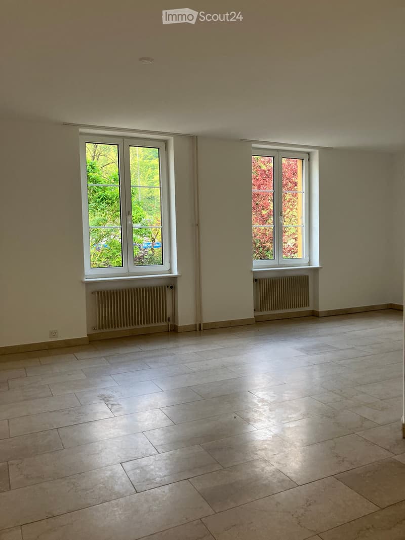 Empty room with tiled floor, large windows, radiators, and neutral-colored walls.