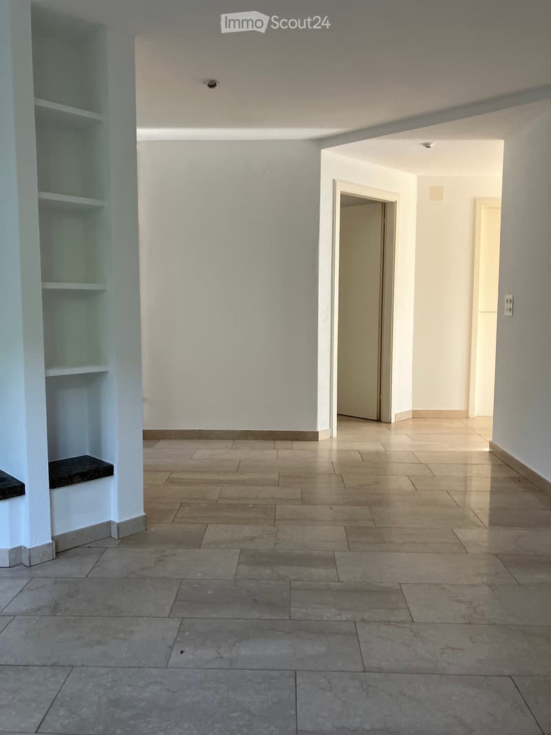Empty hallway with tiled floors, white walls, and a built-in shelf on the left side.
