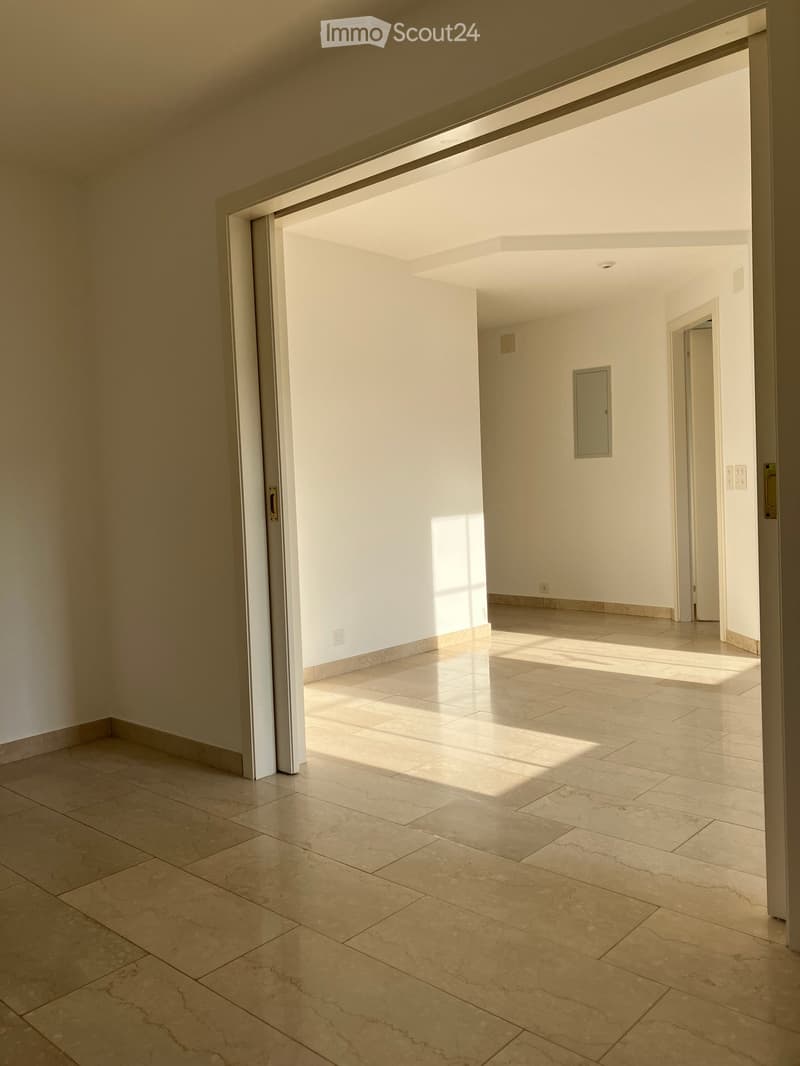 Empty hallway with tiled floors and white walls, featuring an open doorway leading to another room.