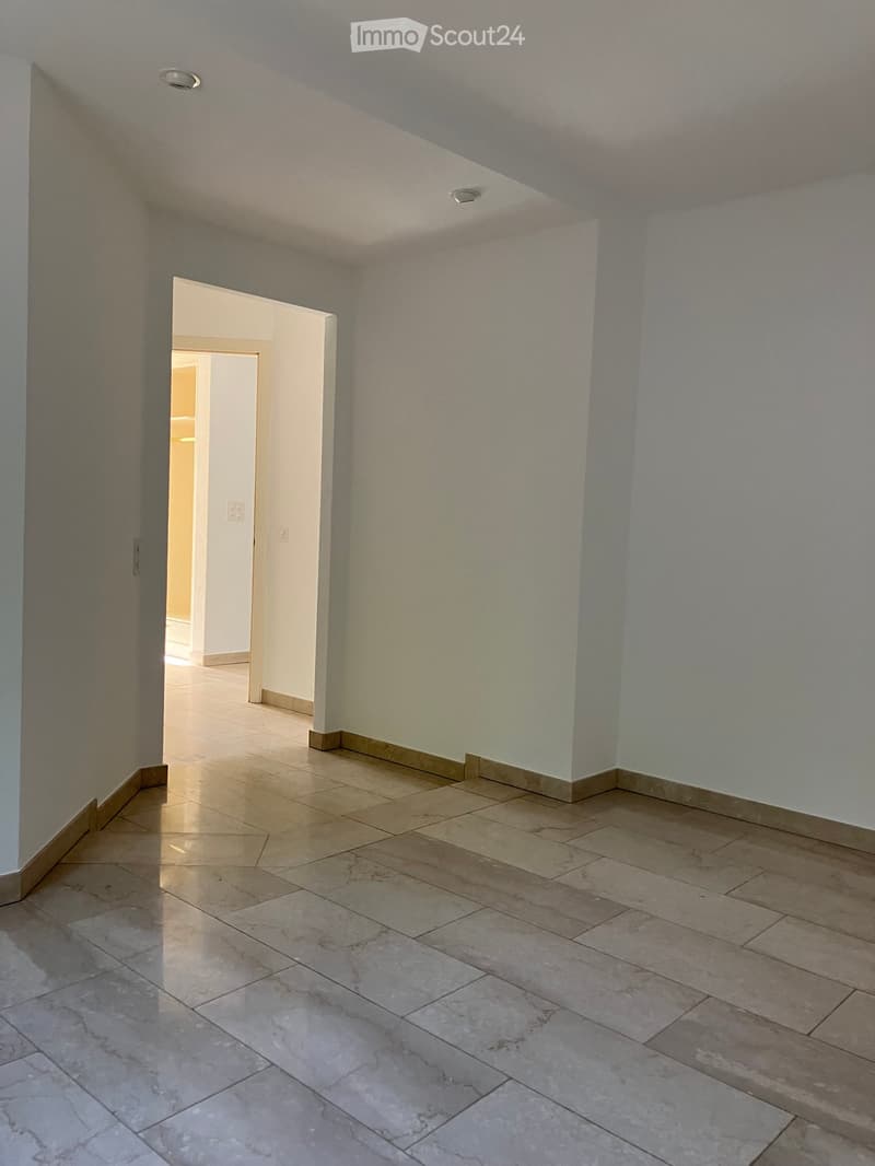 Empty hallway with tiled floor and light-colored walls, featuring a doorway leading to another room.