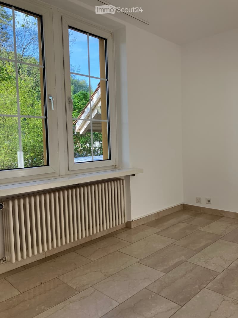 Empty room with beige tiled flooring, white walls, large windows with white frames, and a radiator beneath the windows.
