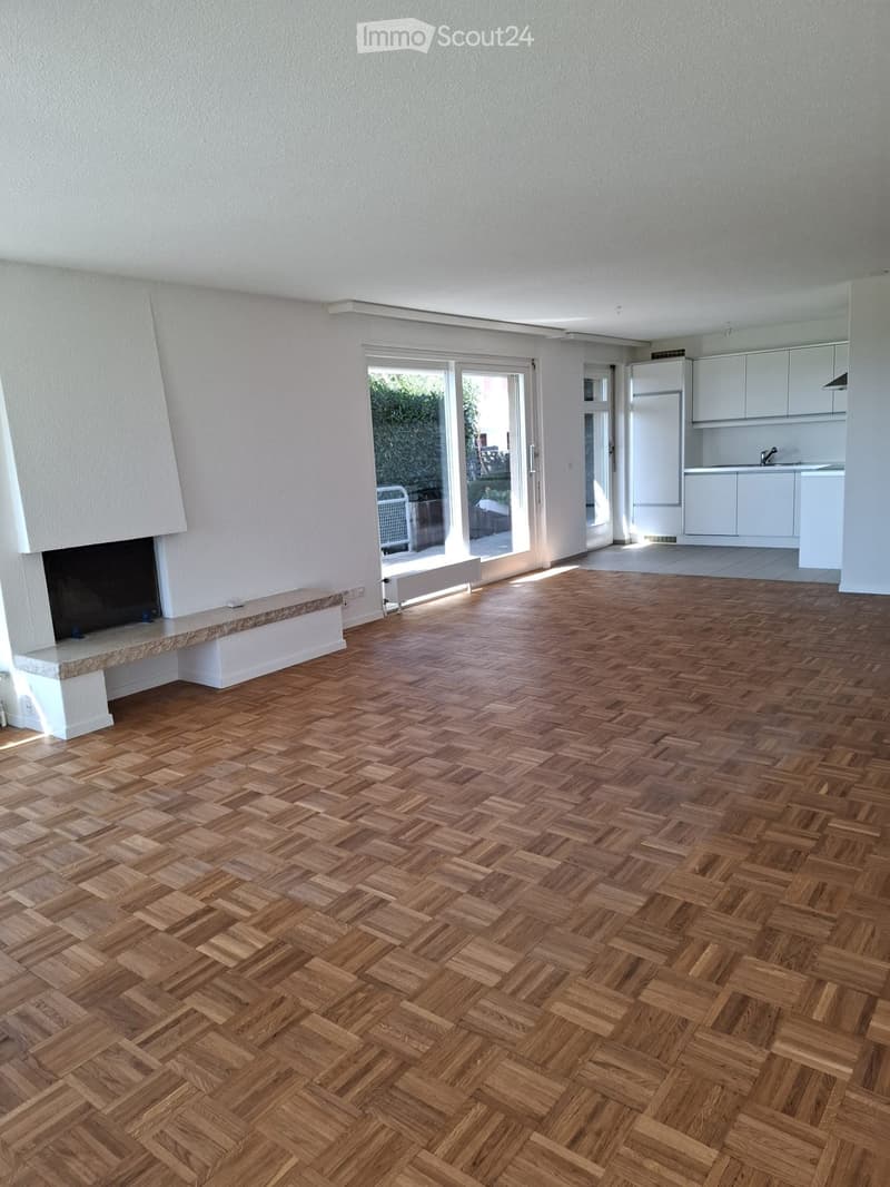 Empty room with herringbone wooden flooring, white walls, fireplace, and large sliding glass doors leading to an outdoor area.