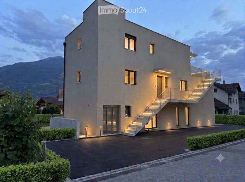 Modern two-story house with a sleek, minimalist design, featuring large windows, a balcony, and a well-lit entrance staircase.