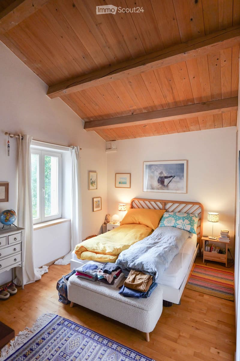 Cozy bedroom with wooden slanted ceiling, bed with colorful bedding, nightstands with lamps, globe, and artwork on walls.