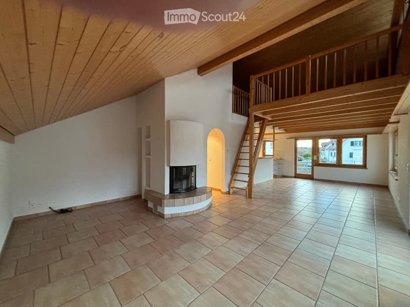 Empty room with exposed wooden beams, tiled floor, and a built-in fireplace. Stairs lead to an upper level.