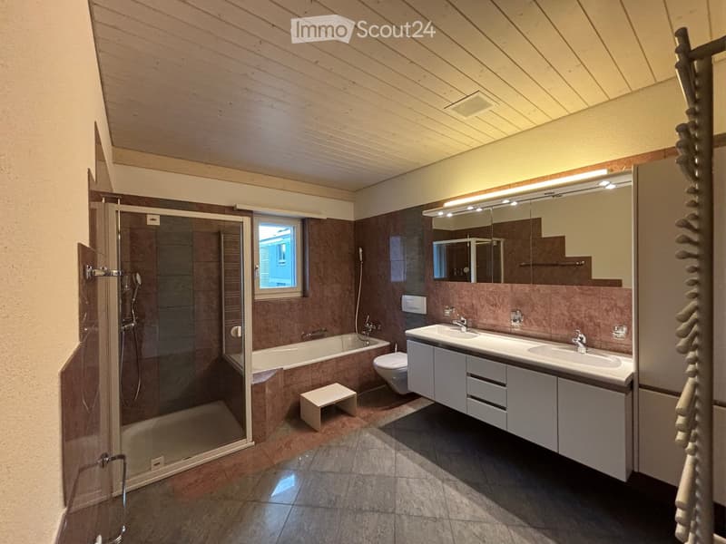 Modern bathroom with a bathtub, toilet, double sink, large mirror, and a glass-enclosed shower. Features a wooden ceiling and warm lighting.