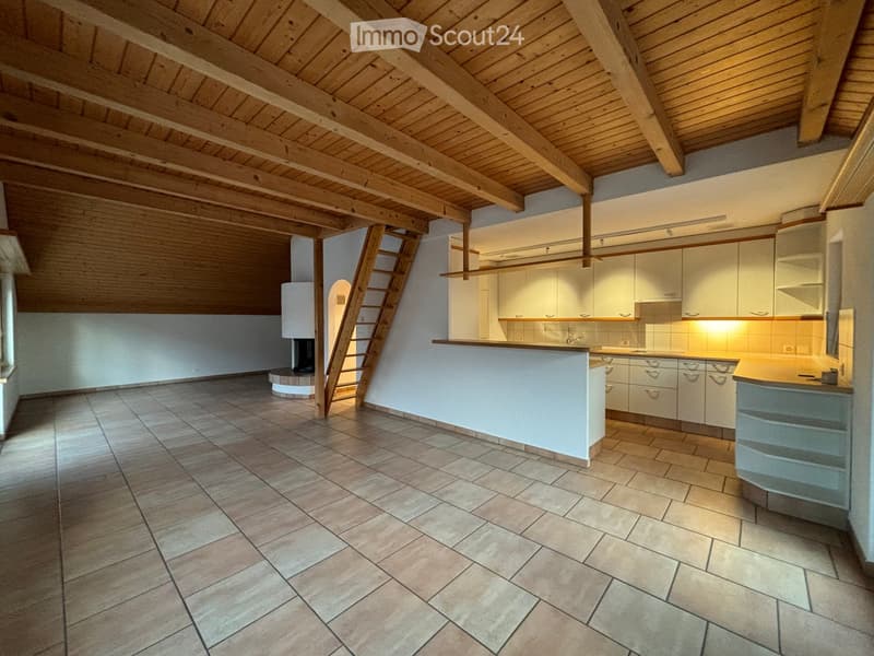 Open kitchen with white cabinets, a central island, and a tiled floor. The space features exposed wooden beams on the ceiling and a ladder leading to an upper level.