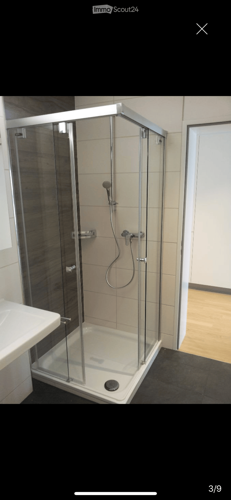Modern bathroom with a glass-enclosed shower, a white sink, and a dark tiled floor.