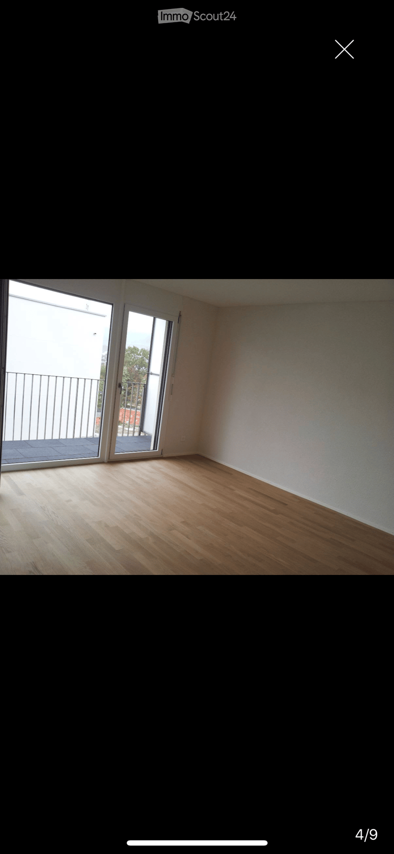 Empty room with wooden flooring, white walls, and large sliding glass doors leading to a balcony.