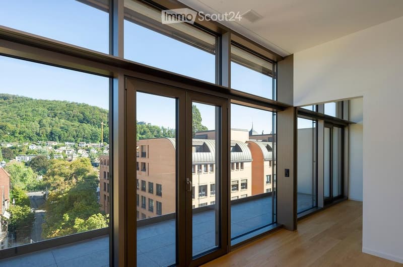 Spacious balcony with large glass doors leading to a tiled floor, offering a scenic view of a cityscape and surrounding greenery.