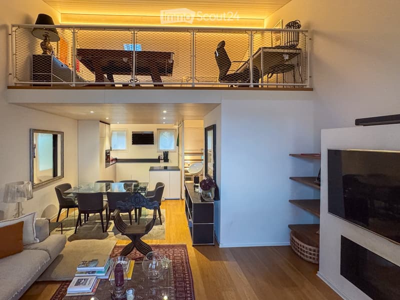 Modern, open-concept living and dining area with a sofa, coffee table, dining table, and kitchen area. Features a fireplace, large TV, and decorative items.