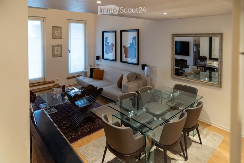 Modern living and dining area with a white sofa, glass coffee table, glass dining table with six chairs, floor lamp, and artwork on the walls.