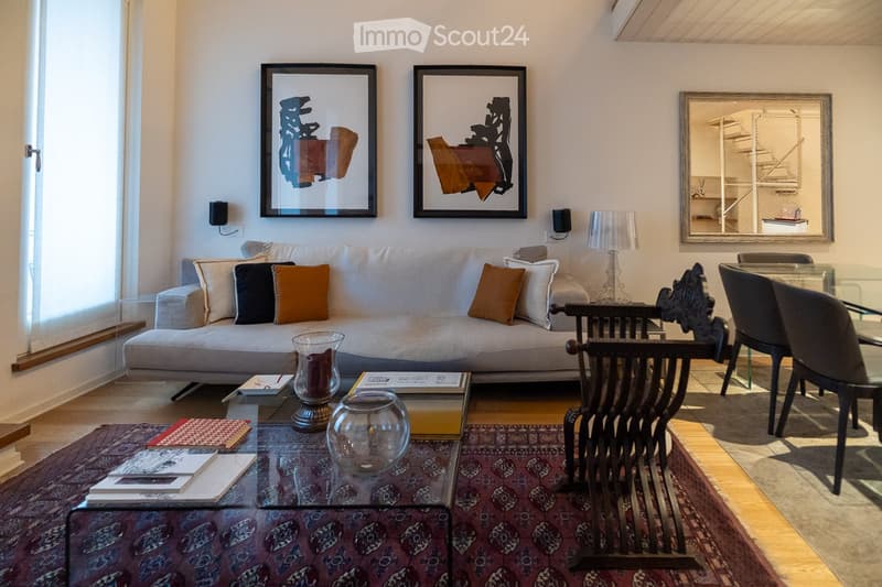 Modern living room with a grey sofa, coffee table, glass vases, books, and a dining area with chairs and a table.