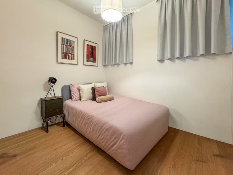 Cozy bedroom with a single bed, pink bedding, nightstand, lamp, and two picture frames on the wall.