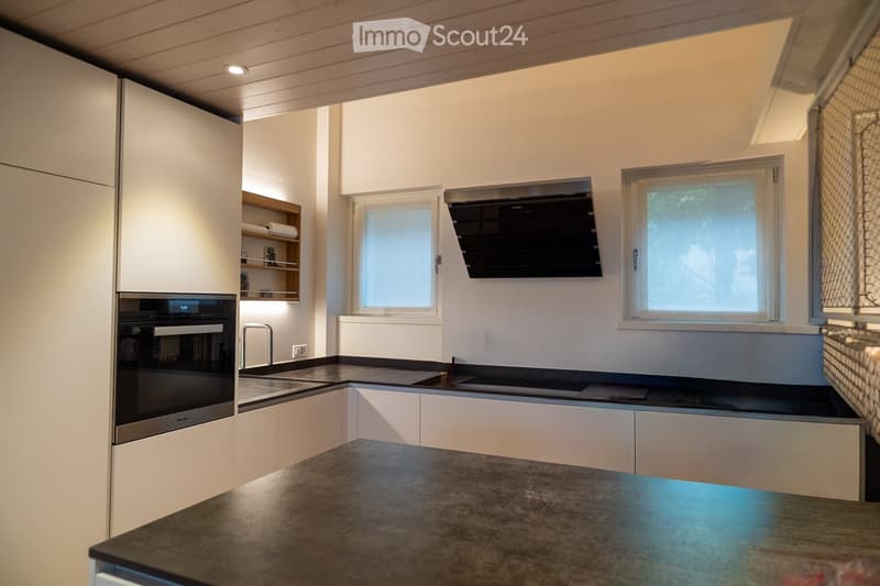 Modern kitchen with white cabinets, stainless steel appliances, and a dark countertop. Features include an oven, sink, and windows for natural light.