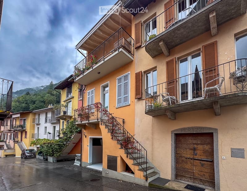 Multi-story residential building with balconies, wooden shutters, and a staircase leading to the entrance.