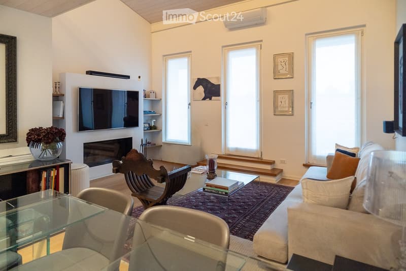 Modern living room with a fireplace, large windows, and a mix of contemporary and traditional furniture including a sofa, coffee table, and wooden chair.