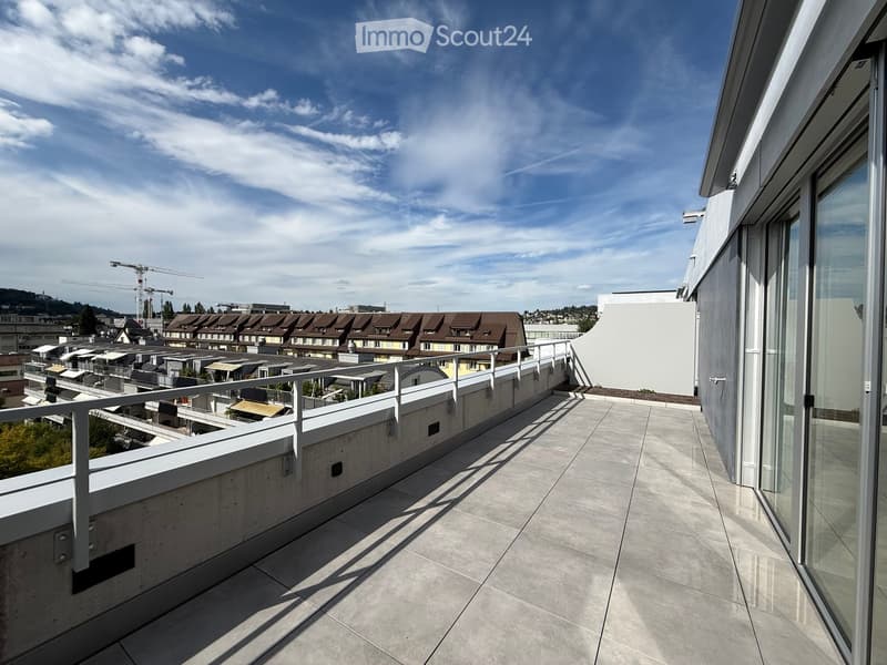 Modern balcony with concrete tiles, white metal railing, and expansive cityscape view under a partly cloudy sky.