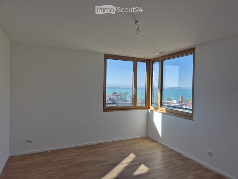 Empty room with wooden flooring, large windows offering a scenic view, and white walls.