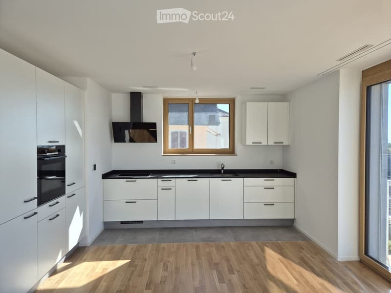 Modern kitchen with white cabinets, black countertops, and wooden flooring. Features a sink, oven, and range hood.