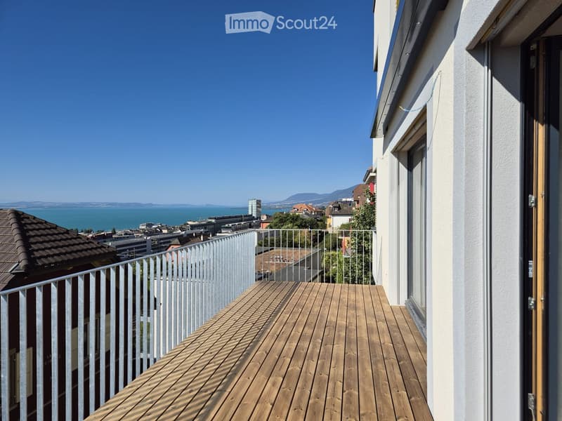 Balcony with wooden decking, metal railing, and scenic view of city and lake.