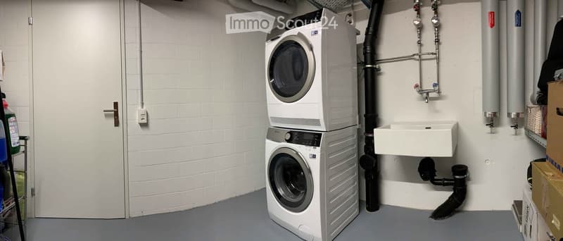 Utility room with a stacked washer and dryer, a white sink, and exposed brick walls.