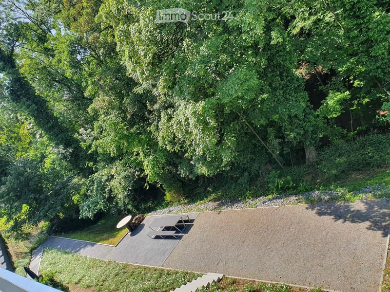 A gravel patio area with a picnic table and bench, surrounded by lush greenery and trees.