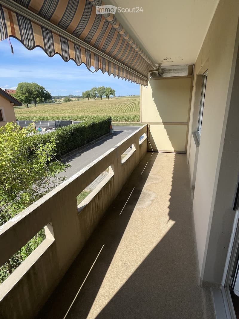 Balcony with striped awning, overlooking a rural landscape with fields and trees.