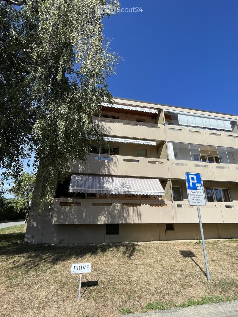 A three-story residential building with beige walls, multiple balconies, and striped awnings. A parking sign and a "PRIVE" sign are visible in the foreground.